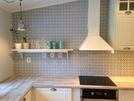 Lyst kjøkken med flislagt mønster på vegg og hylle med kopper og planter